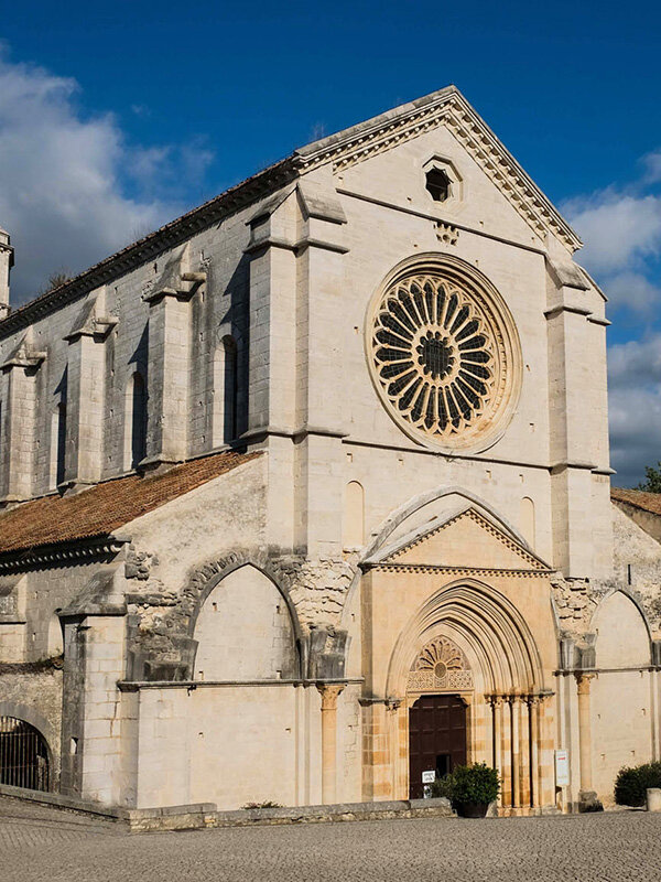Facciata della chiesa dell'abbazia di Fossanova con un rosone e una porta ad arco, sotto un cielo sereno.